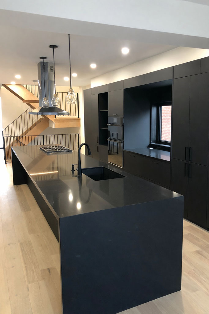 Open concept kitchen with a black waterfall island, pendant lights, and matte-black cabinetry.