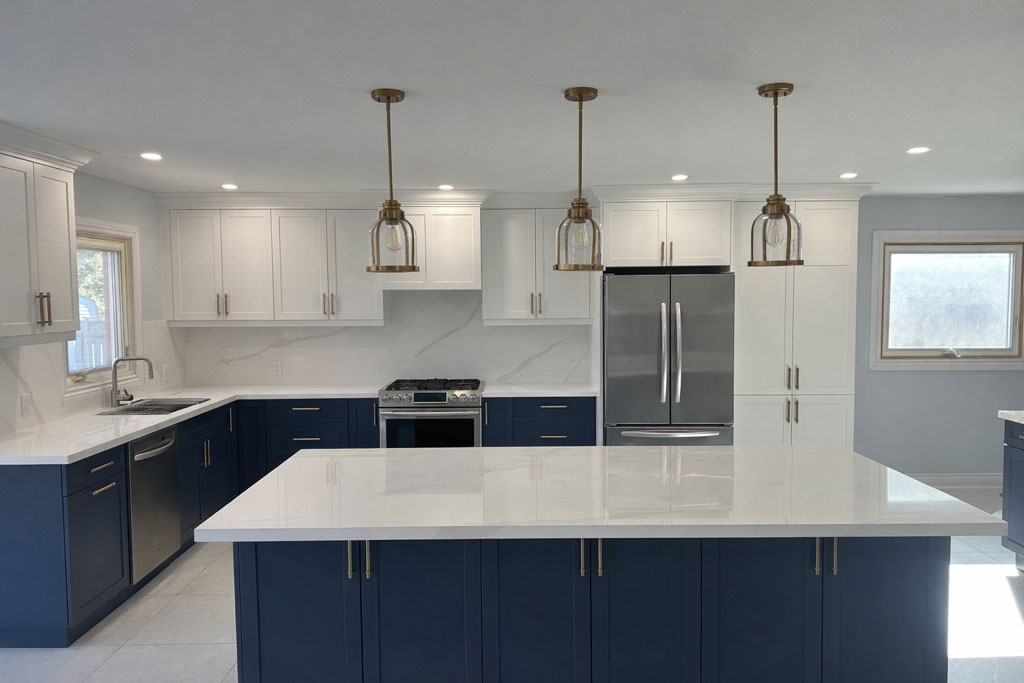 Wide view of a renovated kitchen with a large quartz island, white cabinetry, and pendant lighting.