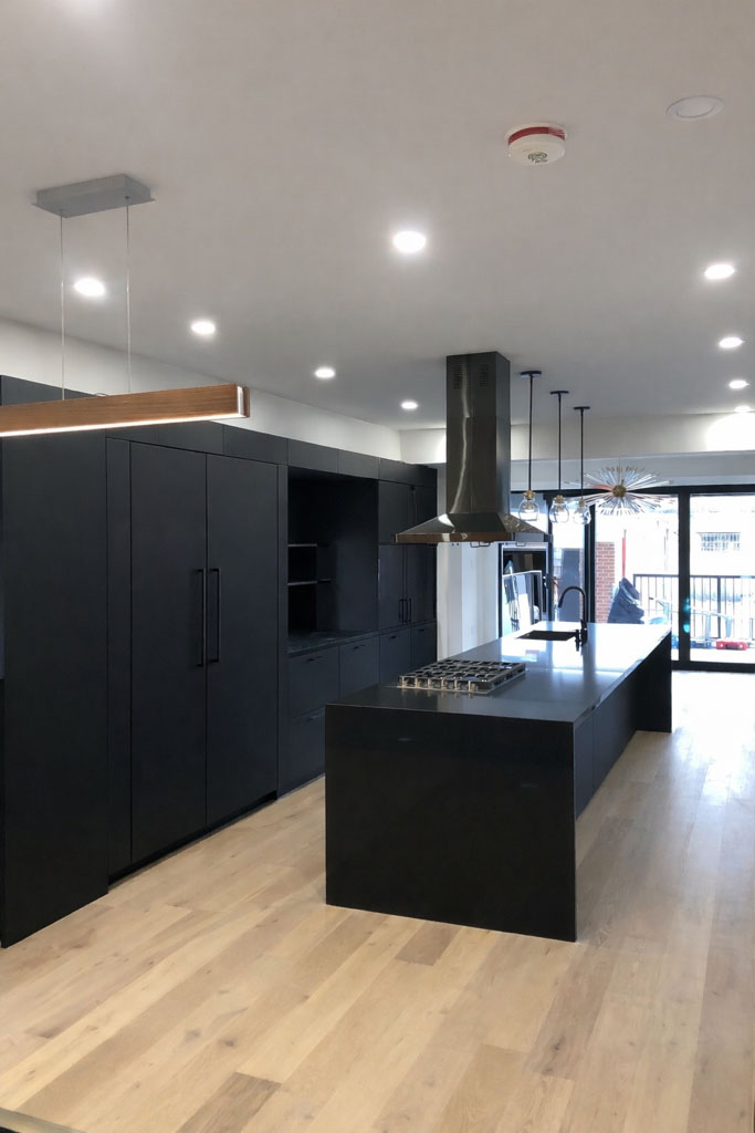 Alternate angle of a modern matte-black kitchen with long island and recessed lighting.