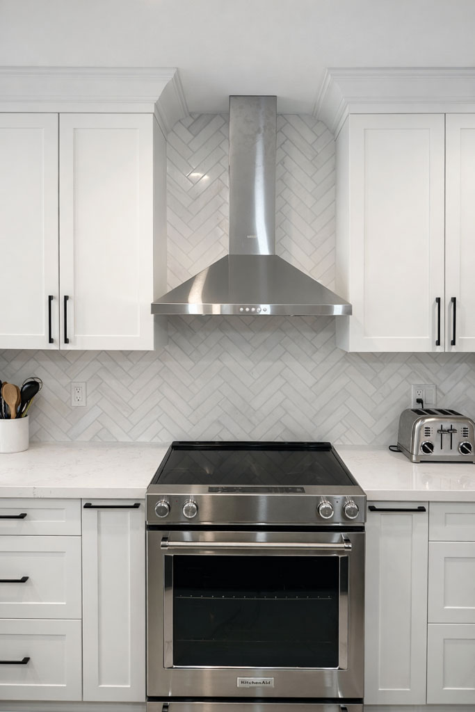 Stainless steel range and hood framed by white shaker cabinets and a herringbone tile backsplash.
